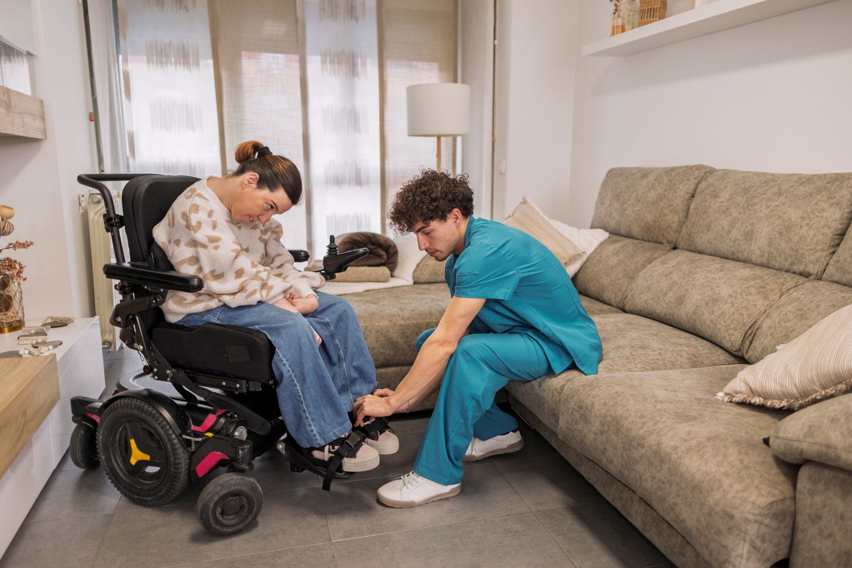 Caregiver assists woman who uses electric wheelchair in her apartment.
